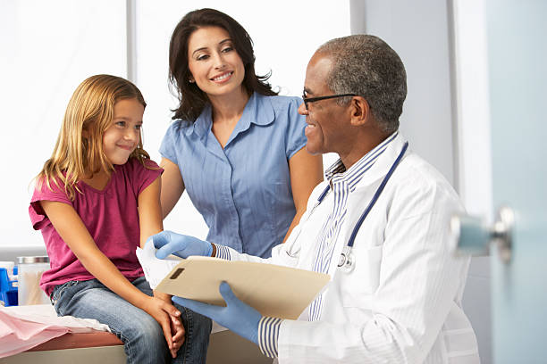 Smiling Doctor In Surgery Examining Young Girl With Mother.